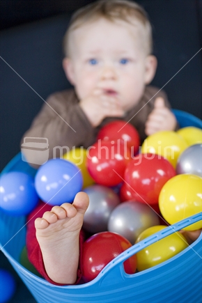 A baby boy sitting in a bucket of colourful plastic balls