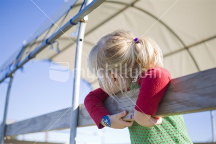 A young blond girl leaning over a fence and looking away