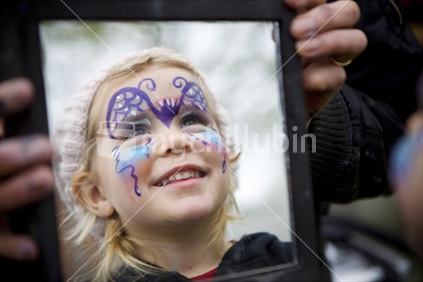 Reflection in a mirror of a young blonde girl with a painted face
