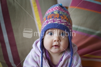 Baby girl with big blue eyes wearing a colourful woolen hat