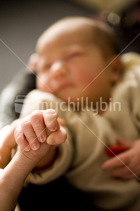 A tiny baby clasping a mothers thumb