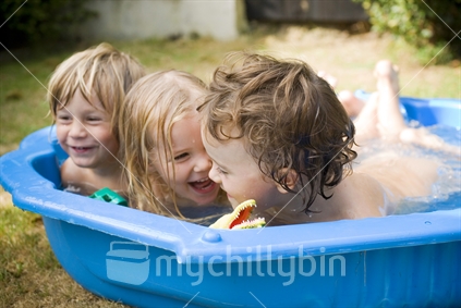 Three young kids having fun in a blue plastic paddling pool