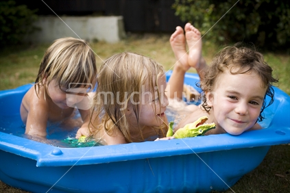 Three young kids having fun in a blue plastic paddling pool