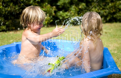 2 blonde kids playing and splashing each other in a paddling pool