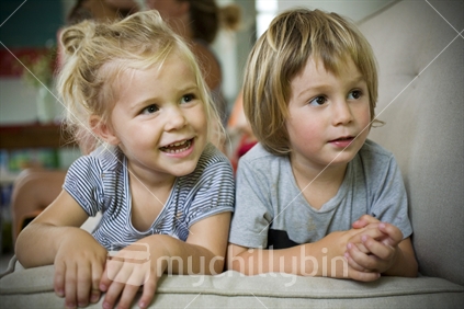 2 blonde children lying on a couch watching TV