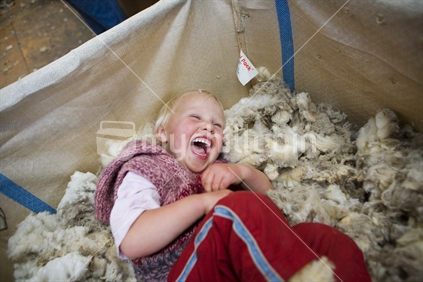 A young blond child laughing in a open wool bale