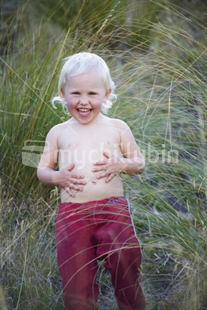 A young blonde child walking in tall tussock grass