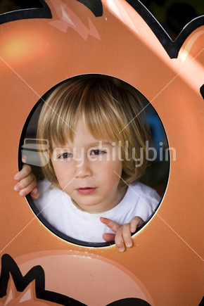 A cute boy peering through a playground cutout