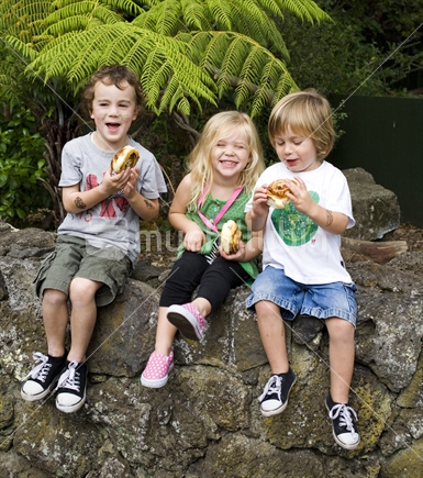 Three kids having a snack on a rock wall