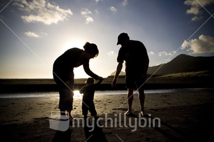 Silhouetted parents holding a childs hand on the beach, Piha, Auckland, New Zealand