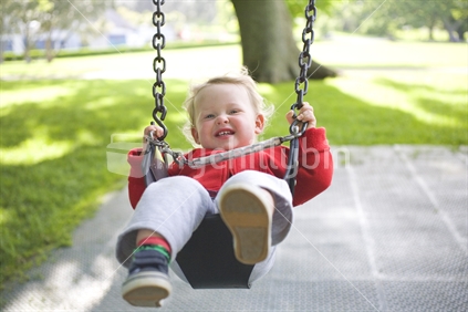 A young blonde boy on a playground swing