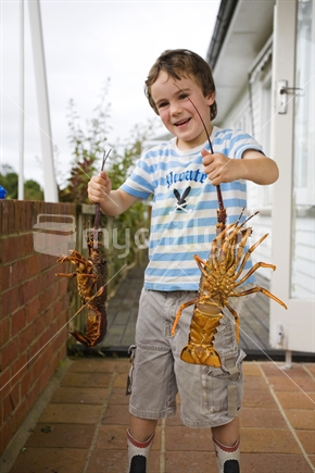 A young boy proudly holding up 2 fresh crayfish