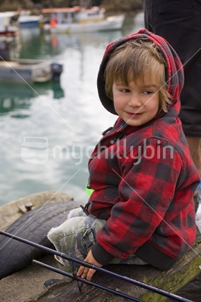 A young boy in a warm hoody fishing off a wharf