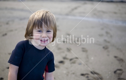 Young smiling boy in a wetsuit on the beach
