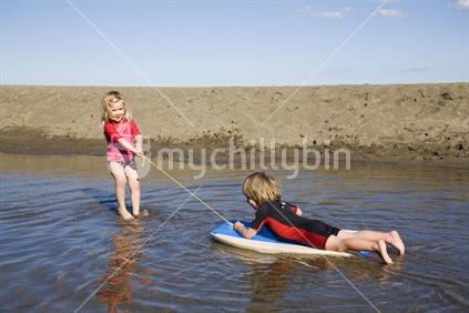 A young girl pulling a young boy along on a boogie board