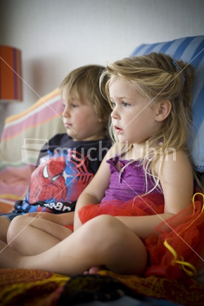 A young boy & girl watching tv together on a couch