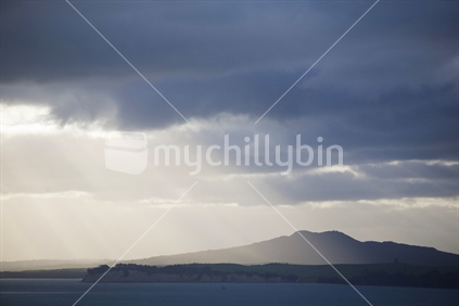 Late afternoon sun rays hitting Rangitito Island through dark rain clouds, New Zealand