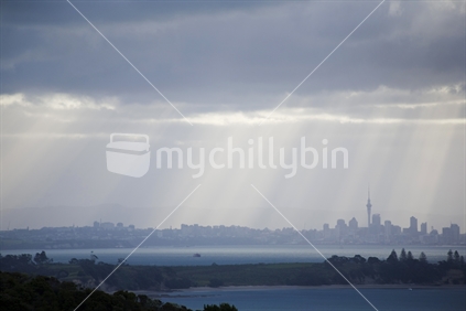 Late afternoon sun rays striking Auckland city through dark rain clouds