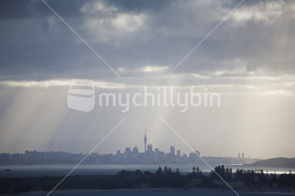 Late afternoon sun rays striking Auckland city through dark rain clouds