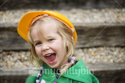 A happy young blonde girl wearing a yellow kids safety hat