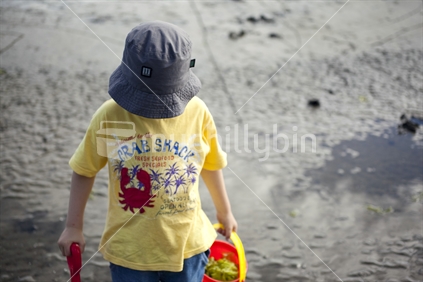 Boy in a hat with a bucket and spade at the beach
