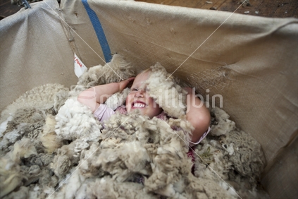 Young blonde child playing in a wool bale at shearing time