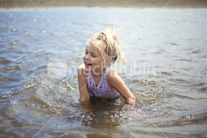 Blonde girl spashing in the water at Piha, Auckland, New Zealand.
