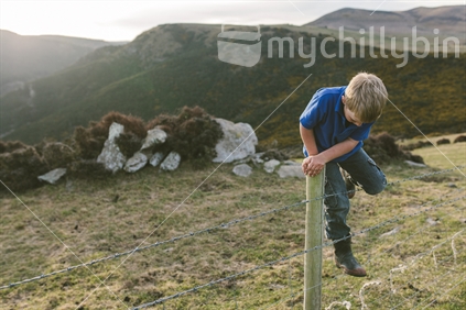 boy climbing over farm fence