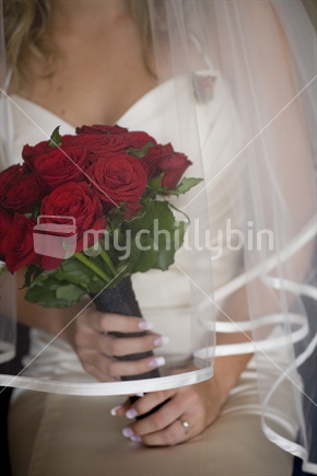 Bride holding a bouquet of red roses under her veil