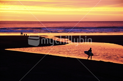 Lone surfer walks home in brilliant sunset, New Zealand