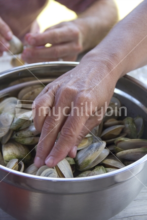 A hand reaches into the bowl for barbequed Tuatua shellfish (selective focus and motion blur)