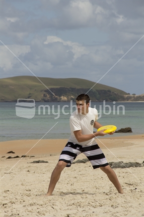 Teenage boy gets ready to throw a frisbee on the beach. 