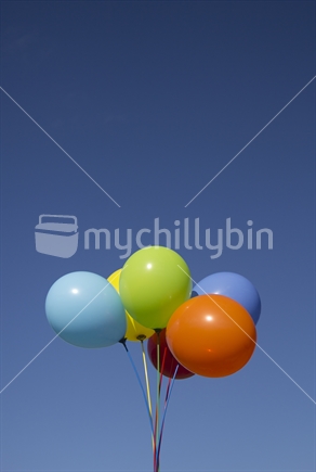 A bunch of bright balloons against a clear blue sky with copy space.  Portrait format.