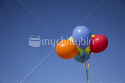 A bunch of bright balloons against a clear blue sky with copy space.  Portrait format.