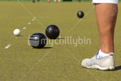 Lawn bowling balls and jack on rink with players leg in foreground.