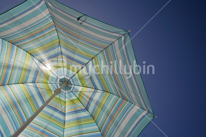 Beach umbrella against blue summer sky, image taken looking up. 