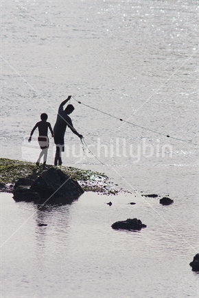 Adult and child fishing with a net off the rocks, silhouette profile.