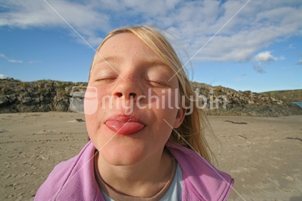 Young girl pokes out her tongue, cheeky face.