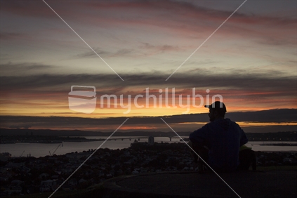 Man watches sunset over Auckland harbour from Devonport, silhouette image.