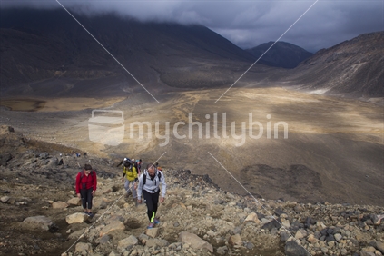 Hikers on the Tongariro Crossing Trail, walking up hill across rocky landscape