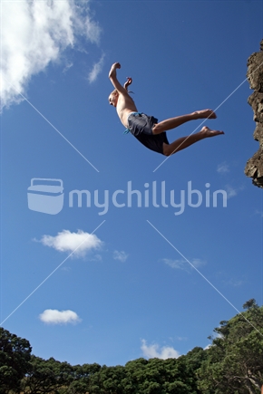 Teenage boy leaping from rock, photographed in mid-air