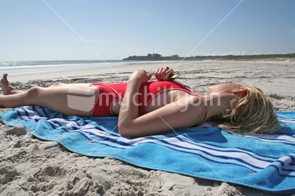 Young blond girl relaxes on the beach, listening to music on her MP3 player, New Zealand
