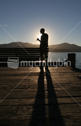 Man in silhouette looking out to sea from Akaroa Wharf, New Zealand