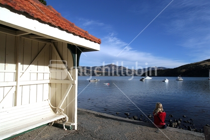 Girl sits looking out over Akaroa Harbour, New Zealand