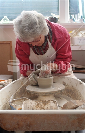 A potter working in her studio, throwing a bowl on electric wheel