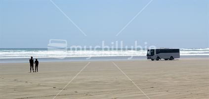 Footsteps in the sand (focus), silhouette swimmers, and bus driving along Ninety Mile Beach, New Zealand