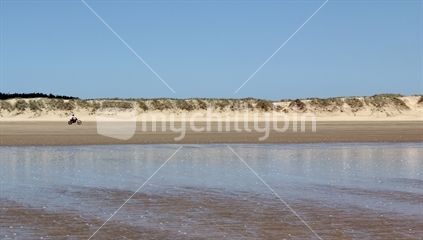 Wet sand foreground (focus), with motorbike driving along Ninety Mile Beach
