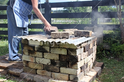 Kiwi ingenuity, home made pit-fire kiln. A woman places bricks on top after the kiln has been lit.