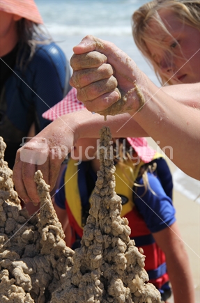 Children make a dribble castle out of sand at the beach.