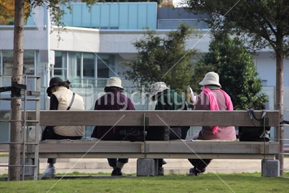 A group of Asian women reading on a park bench, Auckland city. 
